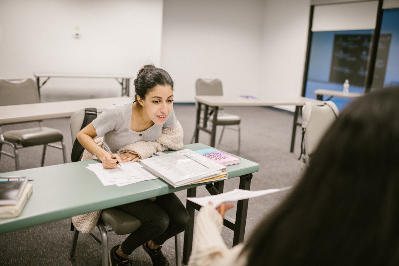A female student in a classroom reviewing exam paper with a classmate, highlighting study collaboration.