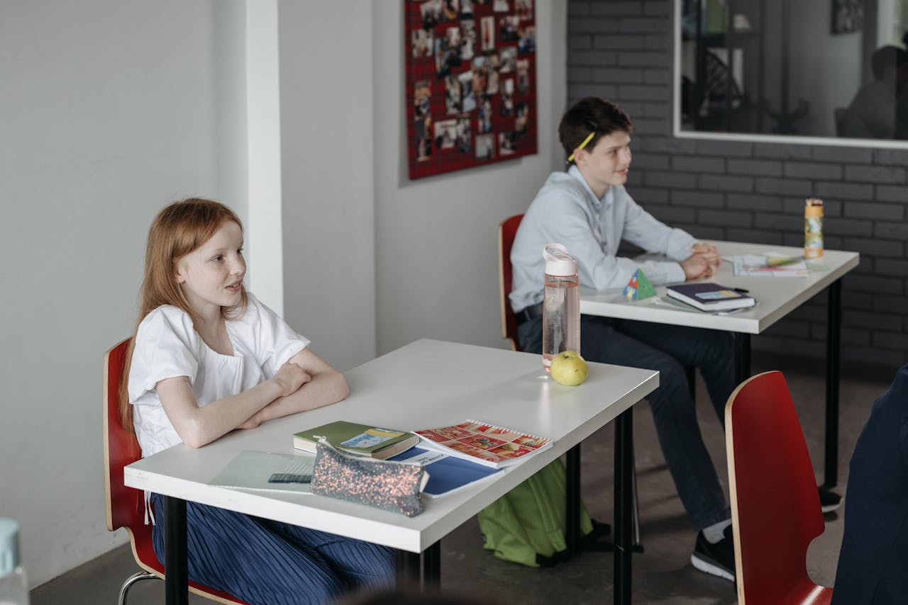 Two children sitting at desks in a classroom, engaged in educational activities.
